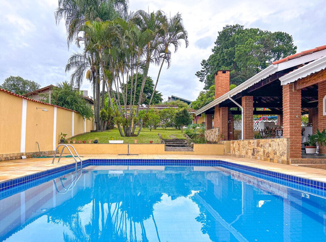 Piscina com água azul cristalina, rodeada por um terraço de tijolos e uma área coberta com telhado.