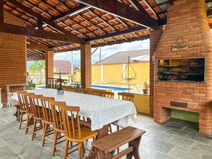 Ein Essbereich im Freien mit Kamin aus Ziegelsteinen, Pool und überdachter Terrasse.
