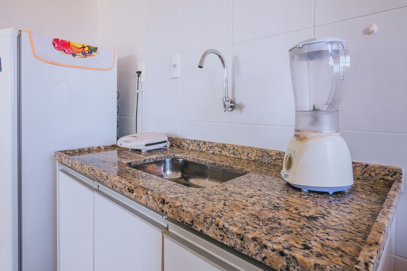 Eine Küche mit Granitarbeitsplatte, Spüle, einem weißen Kühlschrank, einem Mixer und einem Wasserhahn.