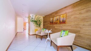 Hall d'albergo moderna con parete decorata in legno, due poltrone bianche, un tavolino rotondo e un quadro di grandi dimensioni.