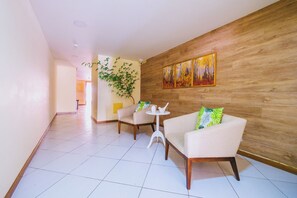 Eine moderne Hotelhalle mit einer Wandvertäfelung aus Holz, zwei weißen Sesseln, einem kleinen runden Tisch und einem großen Gemälde.