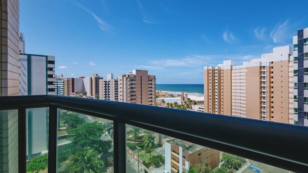 Un edificio alto con diversi piani, vista libera sulla spiaggia e un parcheggio con alcune auto.