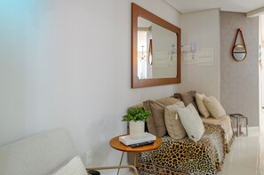 A modern living room with a sofa, a coffee table with a plant, a mirror, and a lamp. - Apto em Penha 400m da Praia Grande | Beto Carrero (Penha)