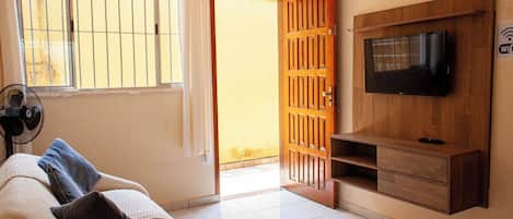Una sala de estar con un sofá, un televisor montado en la pared, una puerta de madera y un ventilador.