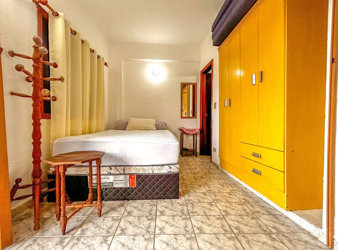 A bedroom with a bed, a wooden chair, a yellow wardrobe, and a mirror on the wall.