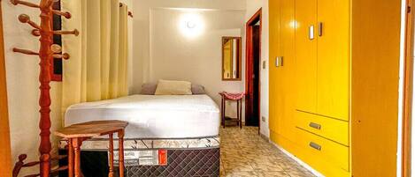 A bedroom with a bed, a wooden chair, a yellow wardrobe, and a mirror on the wall.
