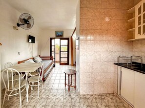 Eine kompakte Küche mit Fliesenrückwand, ein Essbereich mit Tisch und Stühlen, ein kleiner Hocker und ein Deckenventilator.