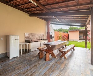 Una veranda esterna con tavolo e panche di legno, un frigorifero bianco e uno schienale in mattoni.