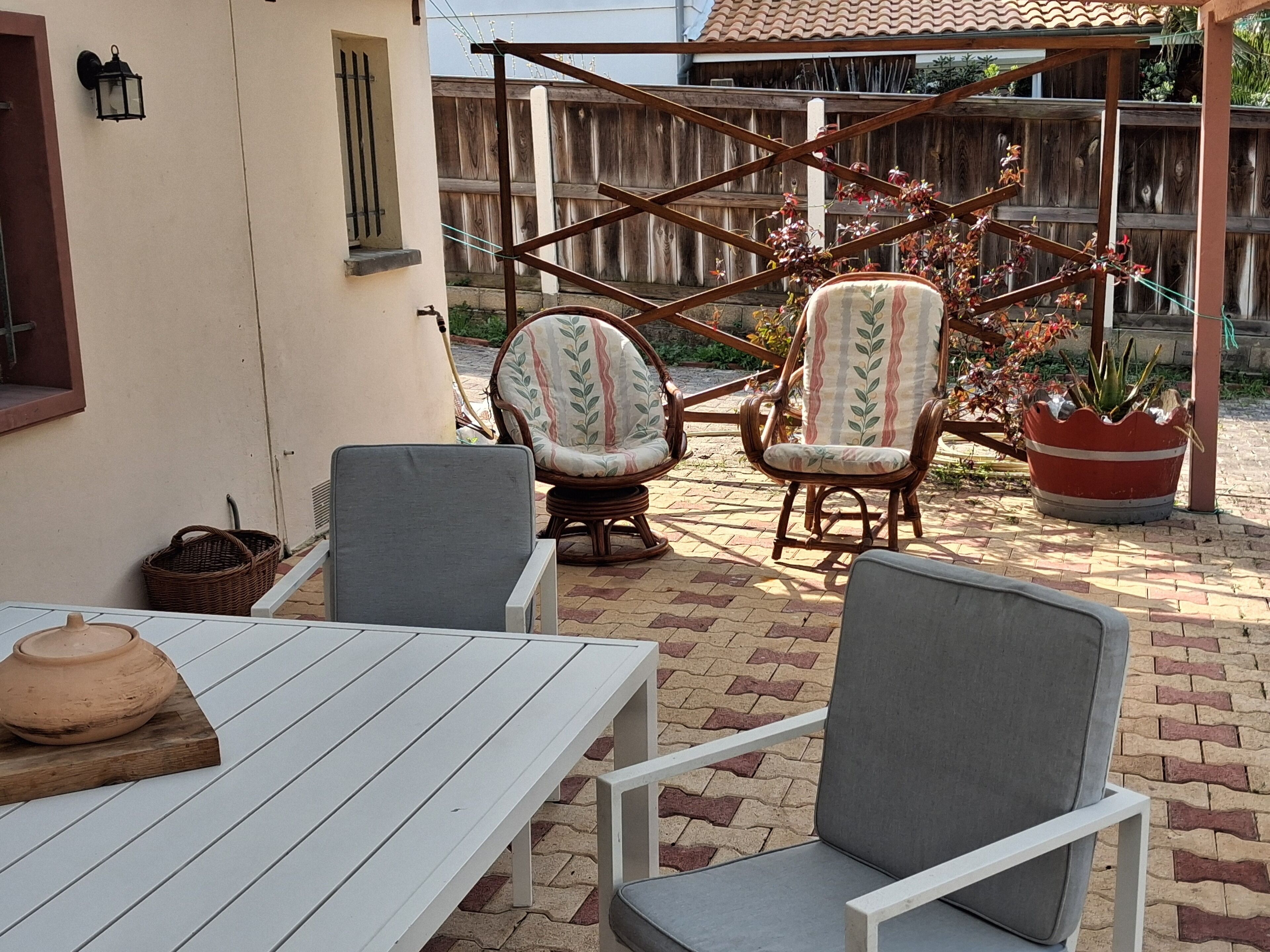 A patio with a white table, two wicker chairs, and a potted plant.