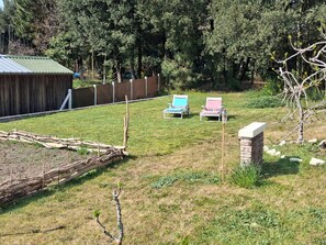 Une cour clôturée avec une construction en bois, deux chaises de jardin et un pilier en pierre.