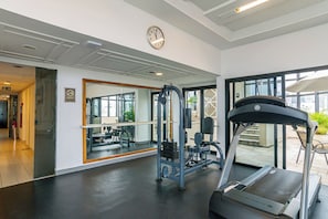 Ein Fitnessstudio mit Laufband, Krafttrainingsgeräten und einem großen Spiegel.