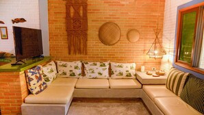 Una sala de estar acogedora con pared de ladrillo, un sofá modular con cojines estampados, un televisor y una lámpara colgante.