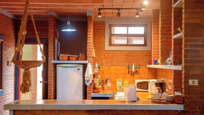 Una cocina con paredes de ladrillo, un colgador para ollas, un refrigerador, un microondas y una ventana sobre el fregadero.