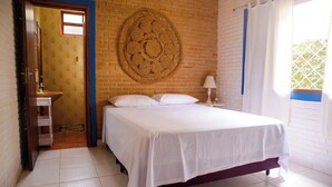 Un dormitorio con cama, un tapiz en la pared, una ventana con cortinas y un baño visible a través de una puerta abierta.