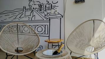 Duas cadeiras de vime com uma pequena mesa de madeira no centro, uma garrafa de champanhe e um mural em preto e branco na parede.