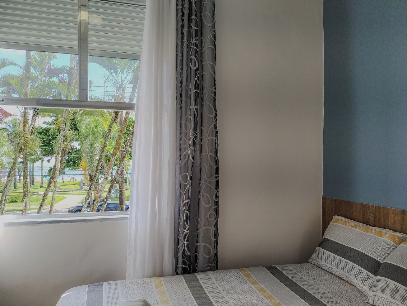Une chambre à coucher avec un lit, des rideaux et une vue sur des palmiers et une route.