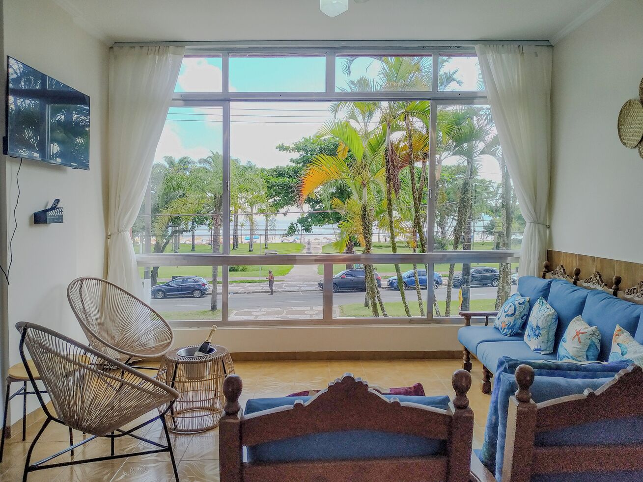 A room with a large window, a blue sofa, wicker chairs, and a wooden bed.