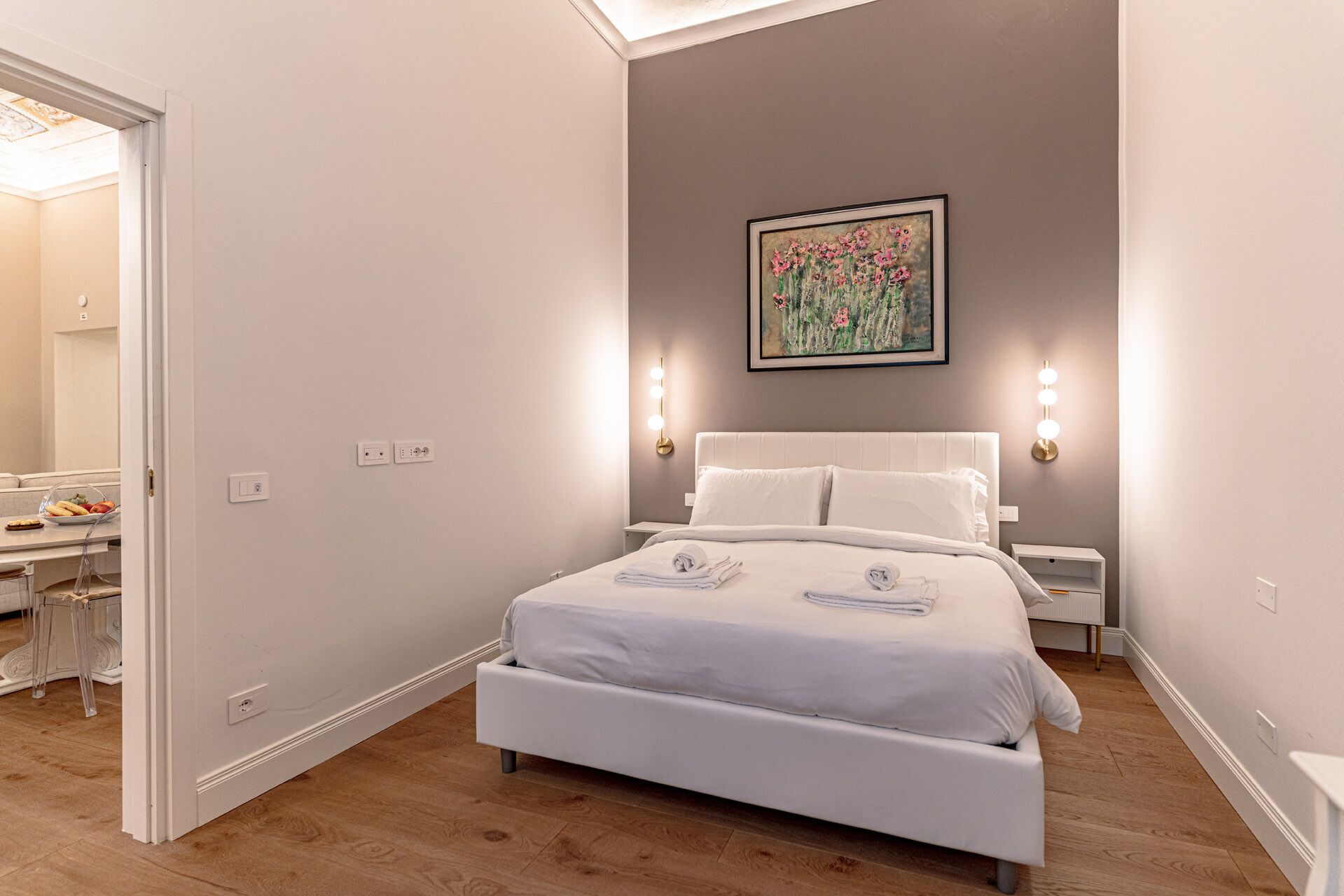 A modern bedroom with a large bed, bedside tables, a painting, and a ceiling light.
