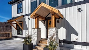 A modern building with a wooden porch, stone pillars, and a number '745' on the wall. - Gorgeous 6BD w/ Hot Tub | Mtn VIEWS + Pool Access (Gatlinburg)