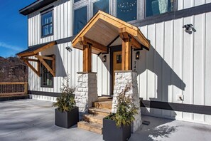 A modern building with a wooden porch, stone pillars, and a number '745' on the wall. - Gorgeous 6BD w/ Hot Tub | Mtn VIEWS + Pool Access (Gatlinburg)