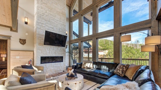 A spacious living room with a fireplace, large windows, and a comfortable seating area. - Gorgeous 6BD w/ Hot Tub | Mtn VIEWS + Pool Access (Gatlinburg)