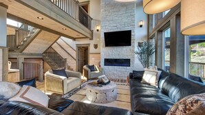 A spacious living area with a stone fireplace, leather sofas, and a high wooden staircase. - Gorgeous 6BD w/ Hot Tub | Mtn VIEWS + Pool Access (Gatlinburg)