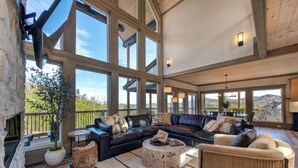 A spacious living room with a large fireplace, leather sofas, a coffee table, and a view of the outdoors. - Gorgeous 6BD w/ Hot Tub | Mtn VIEWS + Pool Access (Gatlinburg)