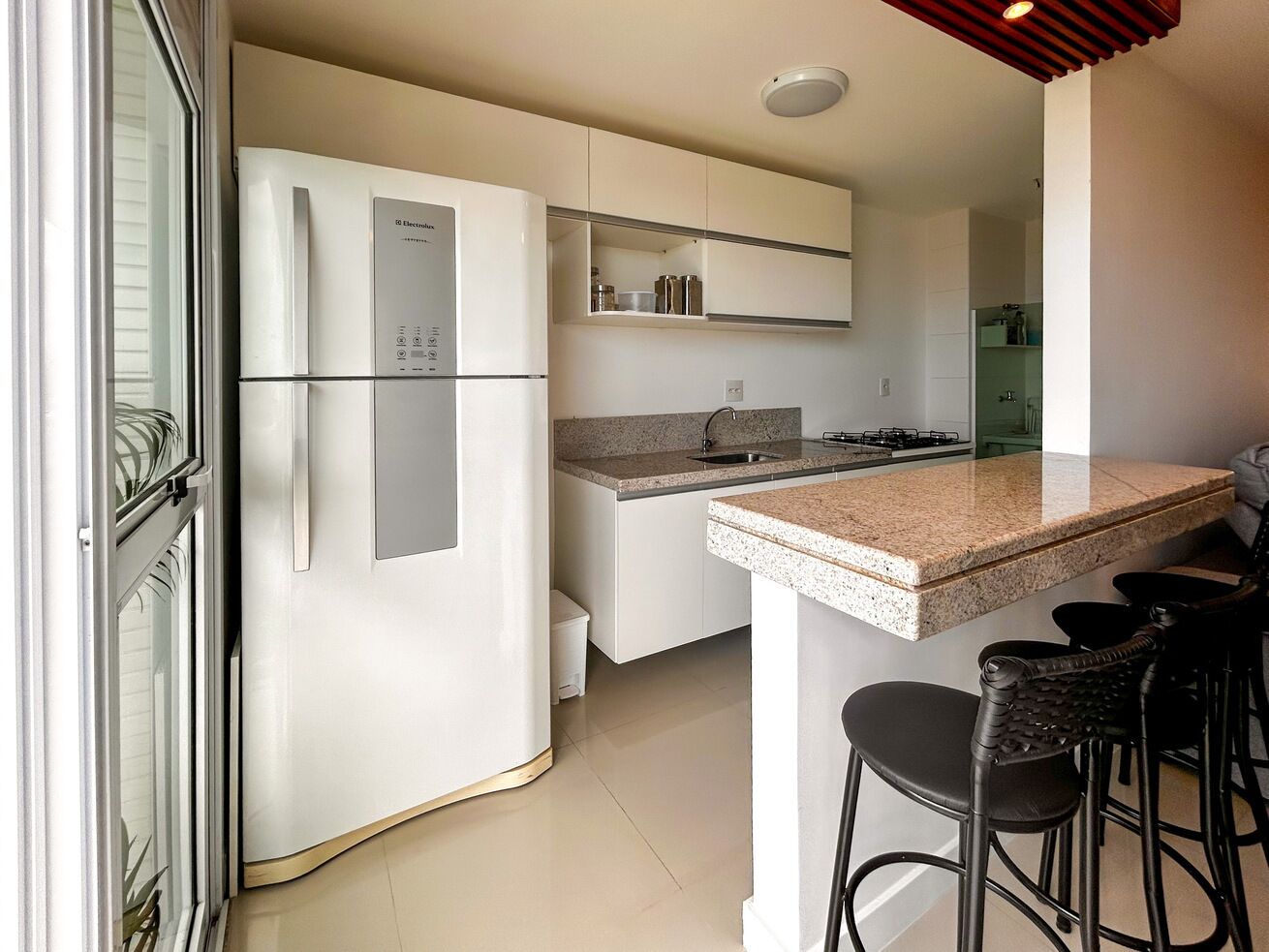 Una cocina moderna con refrigerador empotrado, encimera de granito y taburetes de bar.
