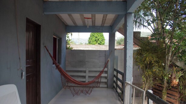 A covered balcony with a hammock, a white chair, and a small table. - Paraty Casa equipada a 10 min do centro histórico (Paraty)