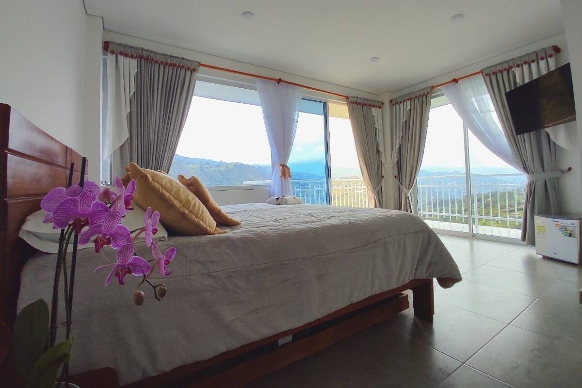 Een slaapkamer met een groot bed, een televisie en een balkon met uitzicht.