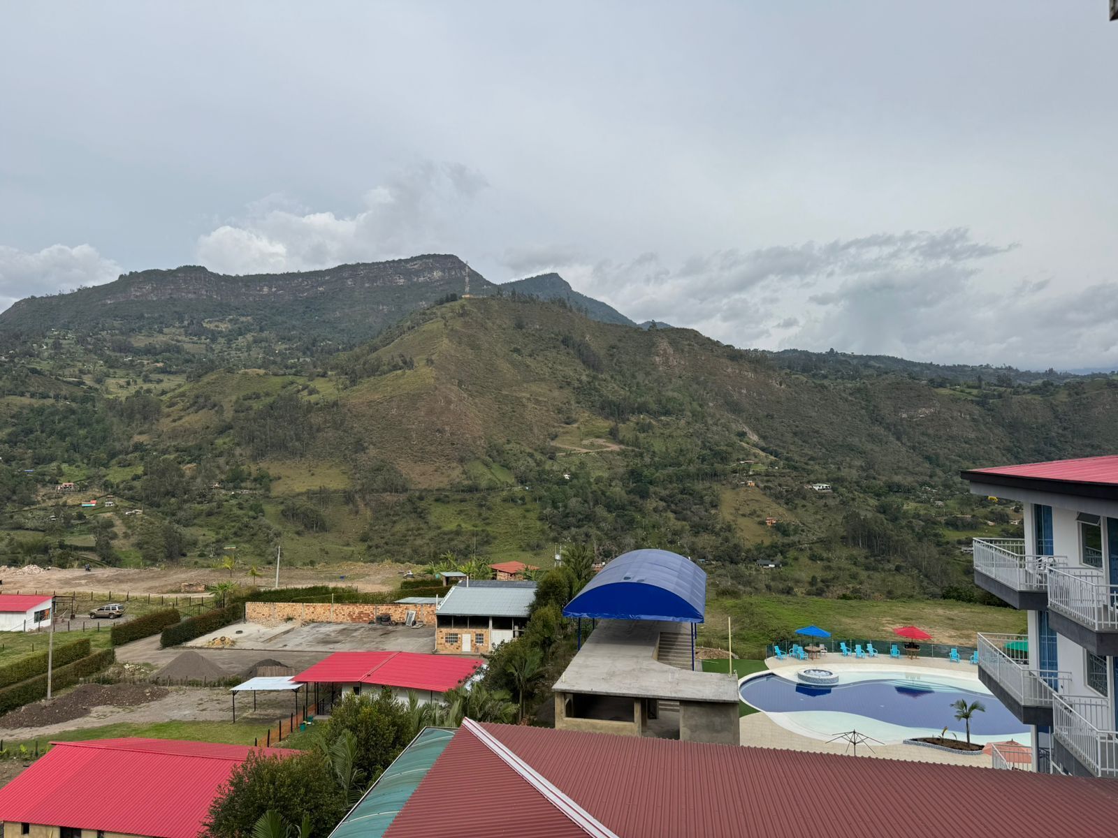 A residential area with a swimming pool, a red-roofed building, and a view of a mountain range.
