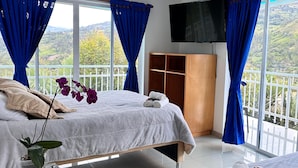 A hotel room with two beds, a TV, a wardrobe, and a balcony with a view of the hills. - Bella vista Hotel  (Choachí)