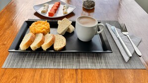A breakfast tray with bread, pastries, and a cup of coffee on a table by a window with a view of a pool and mountains. - Bella vista Hotel  (Choachí)