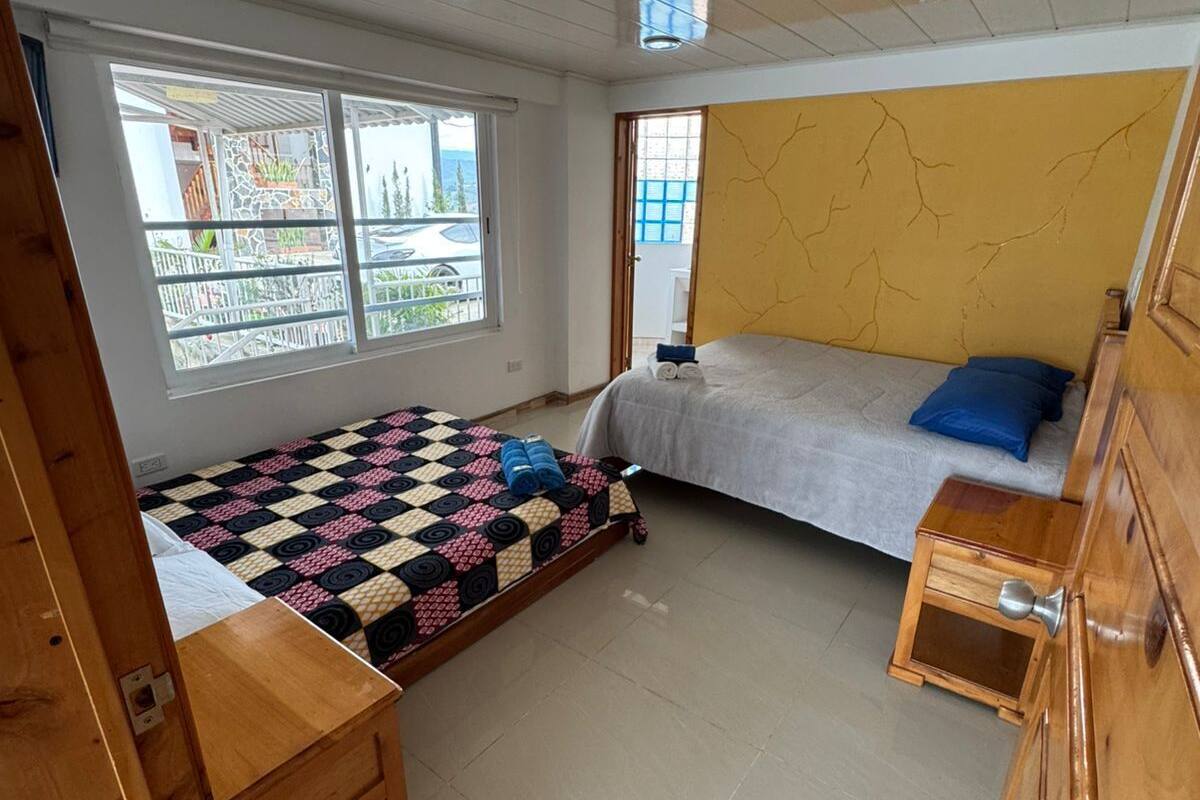 Een slaapkamer met een bed, een klein houten tafeltje, een raam met uitzicht, en een gele muur met een patroon van scheuren.