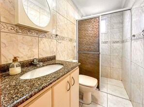 Un baño con lavamanos de mármol, inodoro y zona de ducha con puerta de vidrio.