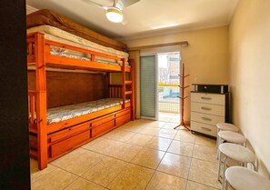 Una habitación con literas, un escritorio con cajones, una silla y vistas a un balcón exterior a través de una puerta.