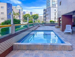 Ein Dachpool mit einer gefliesten Terrasse, umgeben von Hochhäusern und Grünflächen.