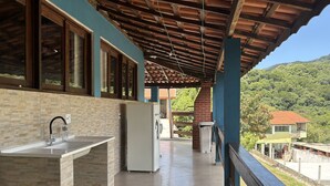 Uma área de cozinha ao ar livre coberta, com pia, geladeira e lixeira.