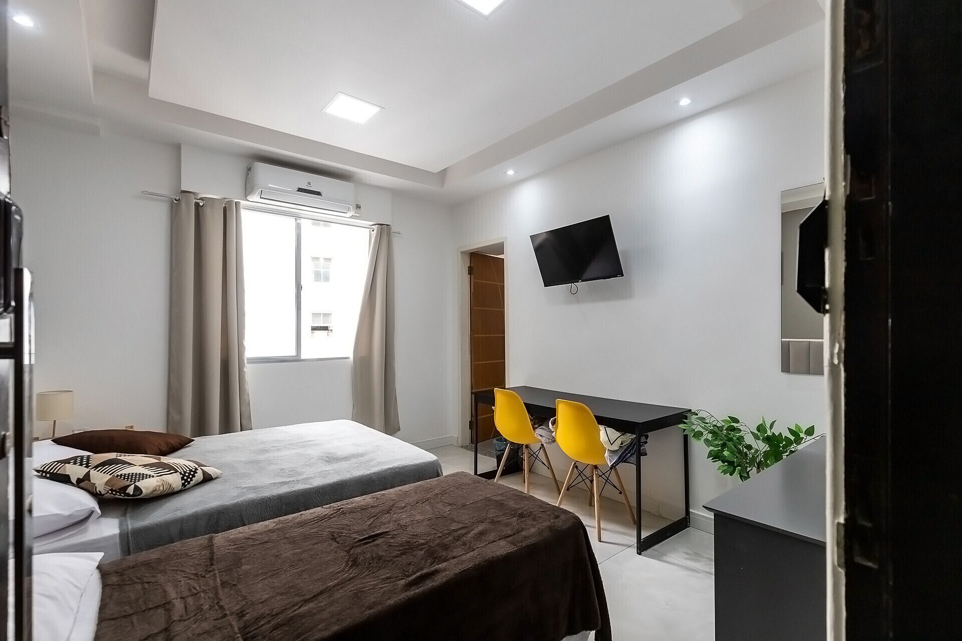 A modern hotel room with two beds, a desk, a TV, and a window with curtains.