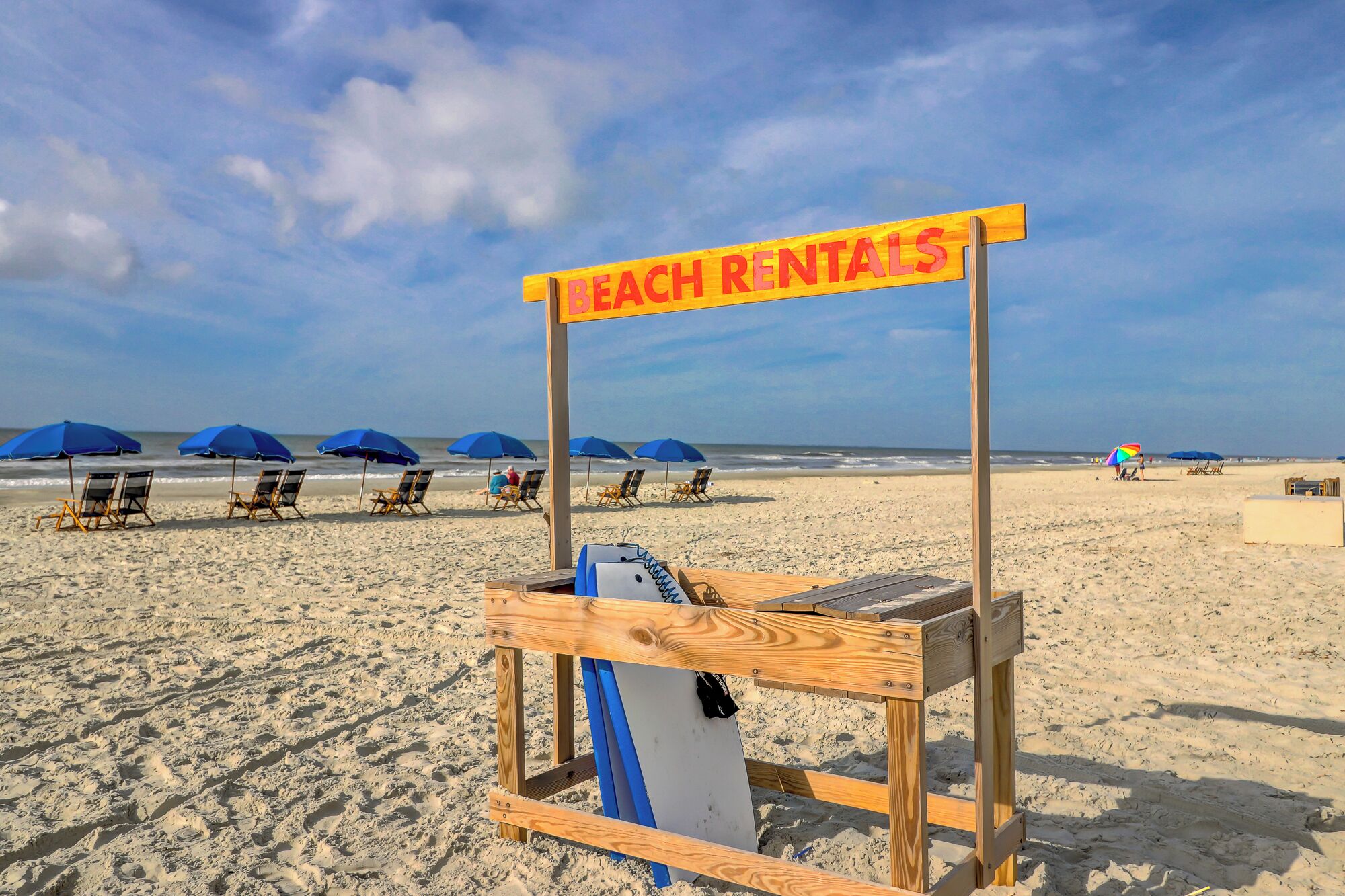 A beach with a rental sign, beach chairs, and umbrellas.