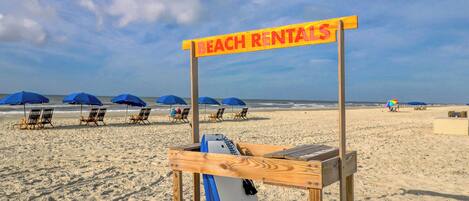 A beach with a rental sign, beach chairs, and umbrellas.