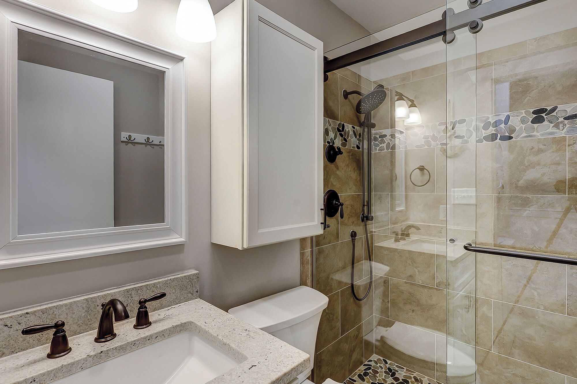 Un baño con ducha de vidrio, un lavamanos blanco y un espejo con luces arriba.