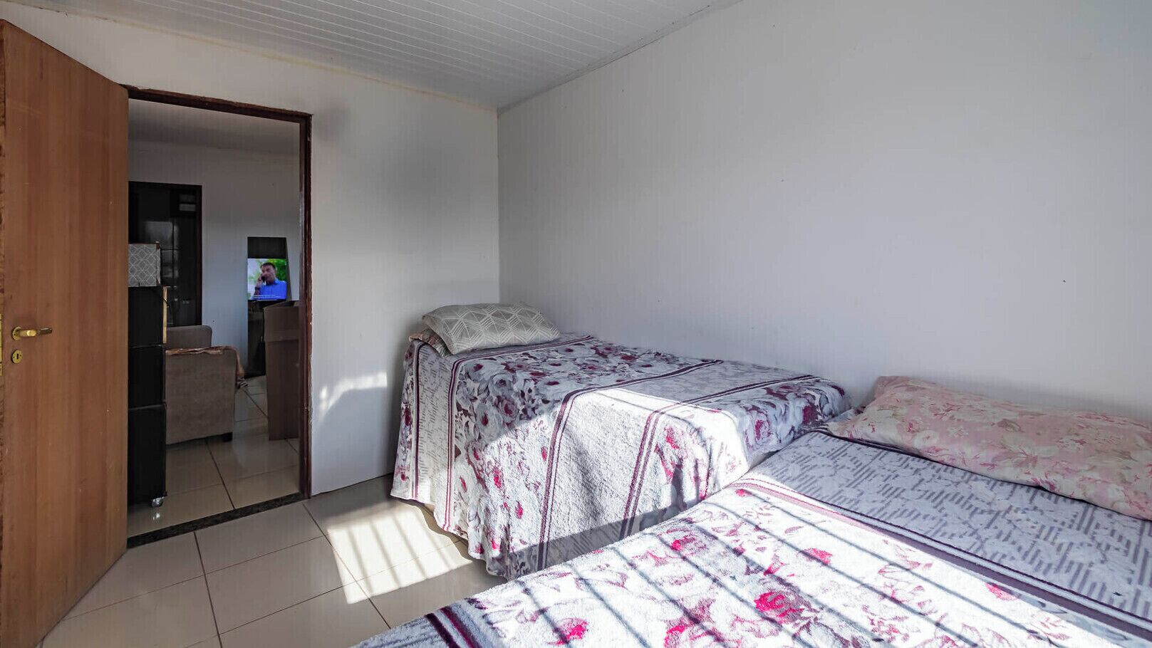 Un dormitori amb dos llits, televisió i una porta que dona a una altra habitació.