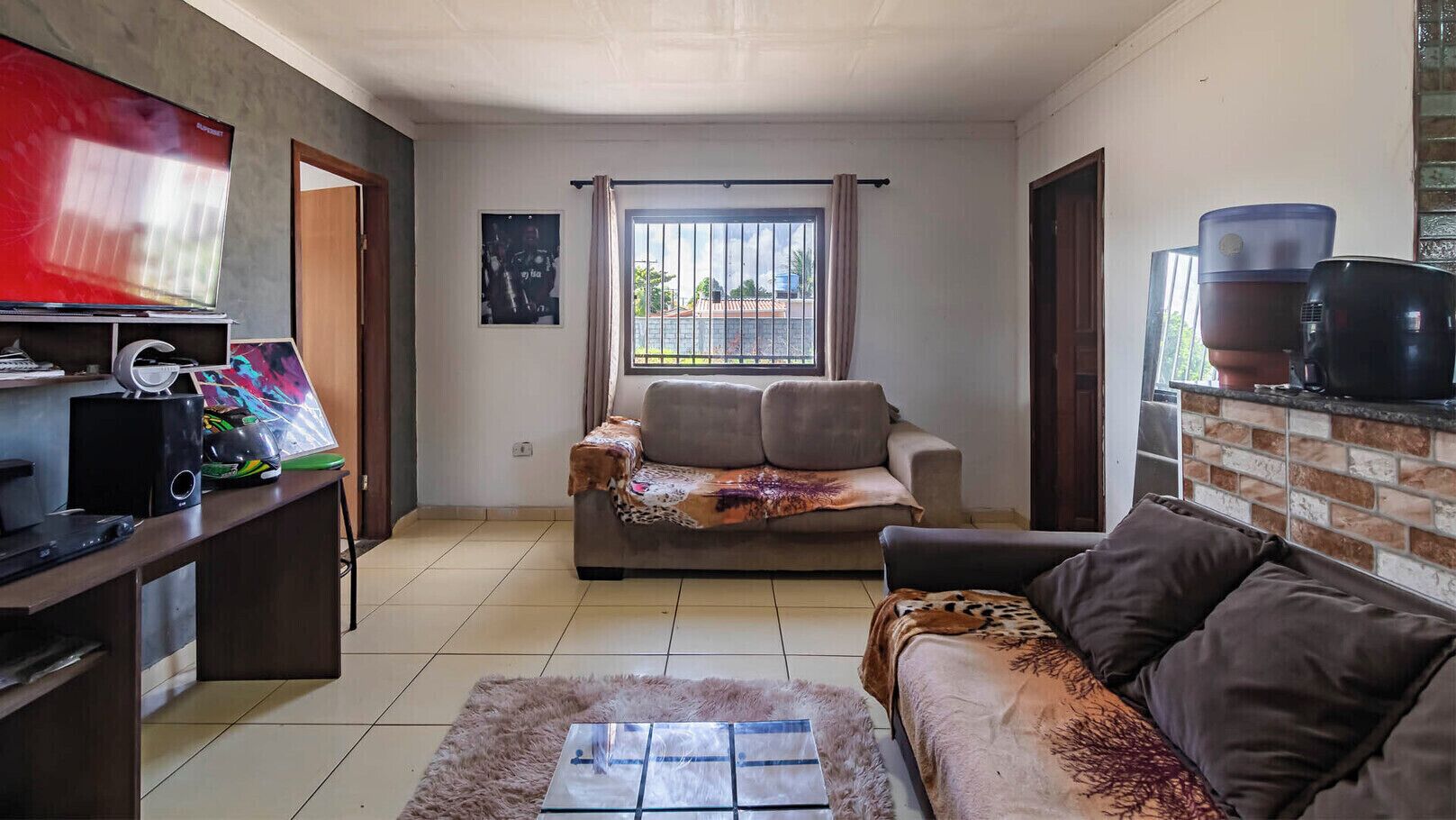 A living room with a sofa, a coffee table, a TV, and a desk with a computer and speakers.