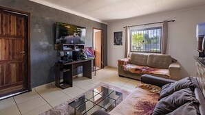 A living room with a sofa, a coffee table, a TV, and a door. - Casa com churrasq e Wi-fi prox. de lindas praias (Santa Cruz Cabrália)