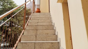 Una escalera conduce a un espacio cubierto con barandilla metálica y vistas a árboles.