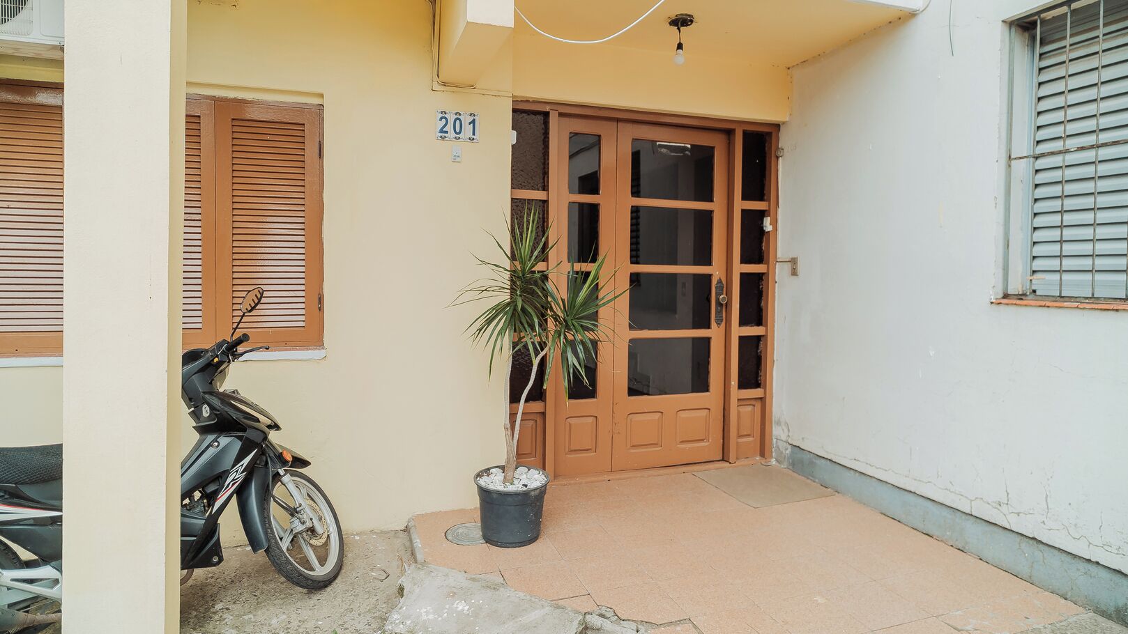 A building with a numbered door, a potted plant, and a parked motorcycle.