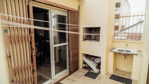 Un pequeño espacio exterior cerrado con puerta corredera de vidrio, una parrilla de metal, un fregadero y una zona con fogata.