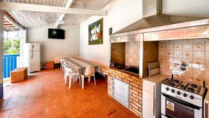 Een buitenkeuken met een gasfornuis, een betegelde spatwand en een eethoek met een tafel en stoelen.