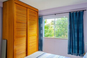 Ein Schlafzimmer mit großem Kleiderschrank, einem Fenster mit Vorhängen und einem Bett mit gestreifter Bettdecke.
